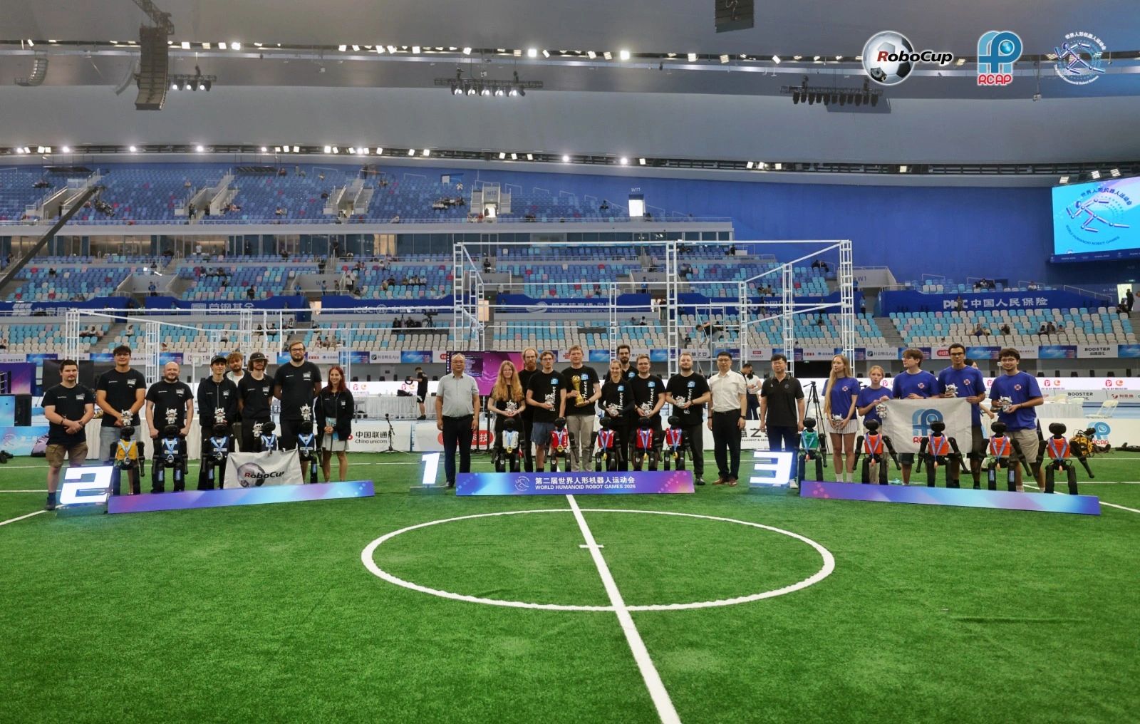 El podio de futbol de humanoides en los World Humanoid Robot Games, con los equipos de pie junto a sus robots sobre el pasto sintético.